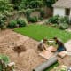 Two people installing a DIY backyard patio with wooden decking and lush garden surroundings.