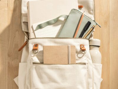 School backpack with notebooks, water bottle, and accessories on wooden desk.