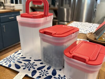 Clear plastic food storage containers with red lids on a kitchen table.
