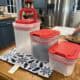 Clear plastic food storage containers with red lids on a kitchen table.