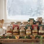 7 Assorted layered soup mix jars on a windowsill with snow outside.