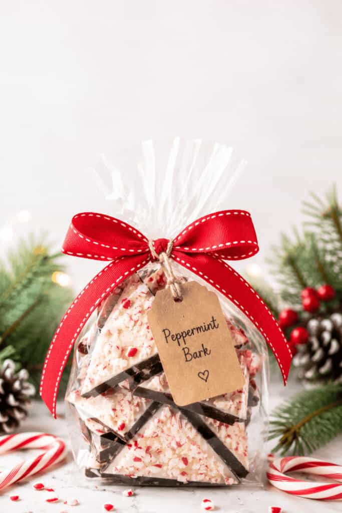 25 Homemade Food Gifts for Christmas That Everyone Loves 5 Festive peppermint bark gift wrapped with a red ribbon and holiday decorations.