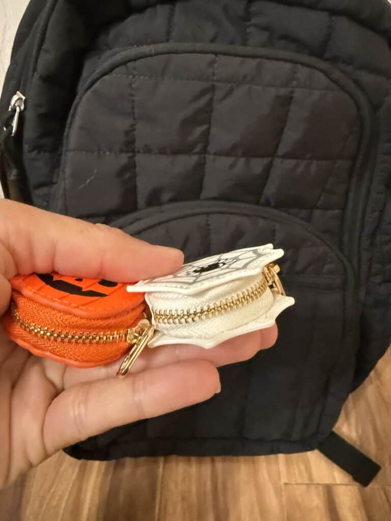 15 Backpack Charm Ideas: Easy DIY + Where to Find the Cutest Ones 6 Hand holding two small Halloween-themed coin purses in front of a backpack.